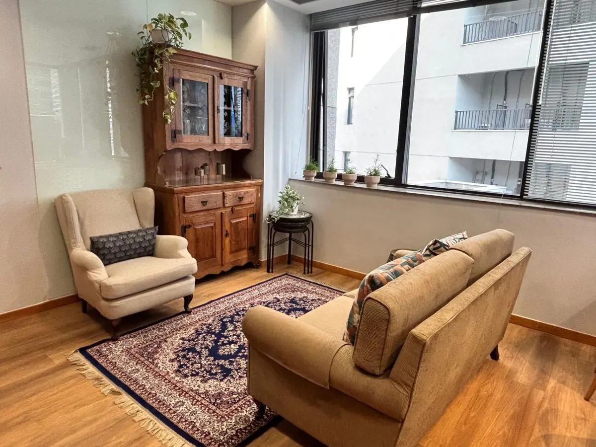 Sala da clínica com poltrona, sofá, cristaleira de madeira e janela ampla